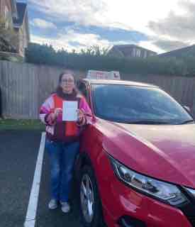 Successful driving student holding certificate beside the AG Driving School car.